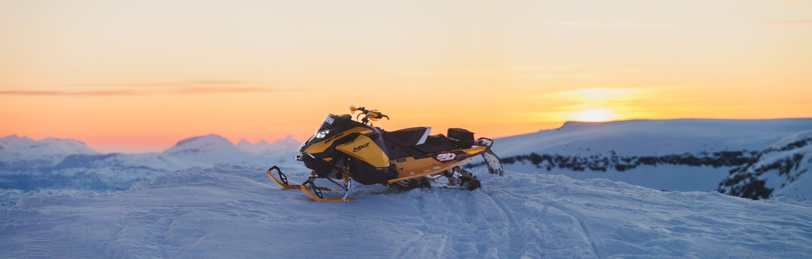 Gul Ski-Doo MXZ på fjället i solnedgången